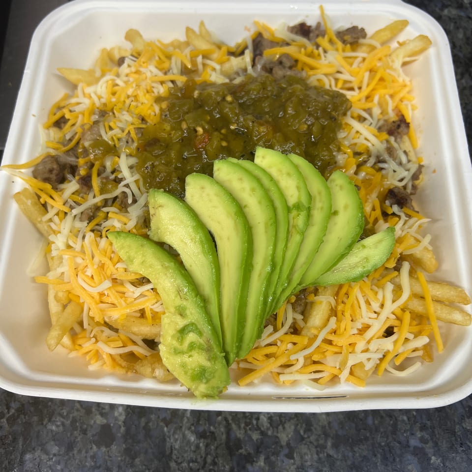 Loaded fries with cheese, ground beef, green salsa, and sliced avocado in a white takeout container.