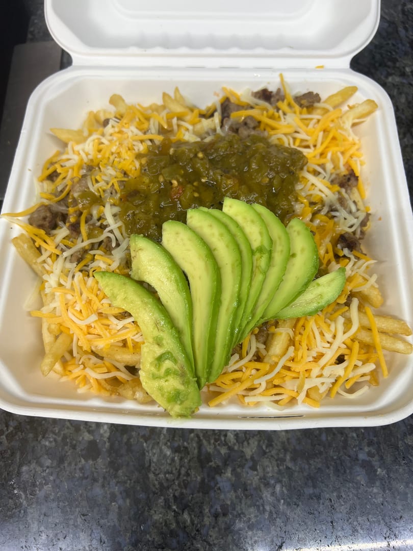 Loaded fries with cheese, ground beef, green salsa, and sliced avocado in a white takeout container.