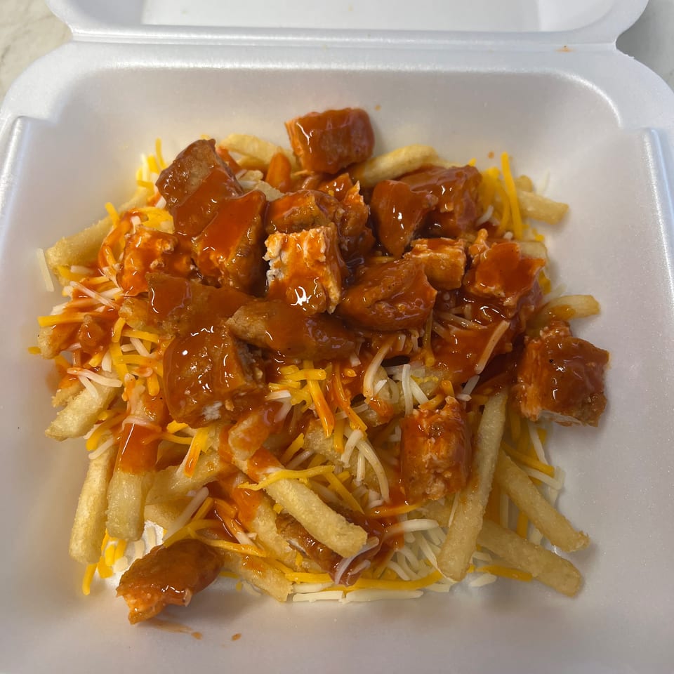 Fries topped with melted cheese and chicken pieces drizzled with orange sauce in a white takeout container.